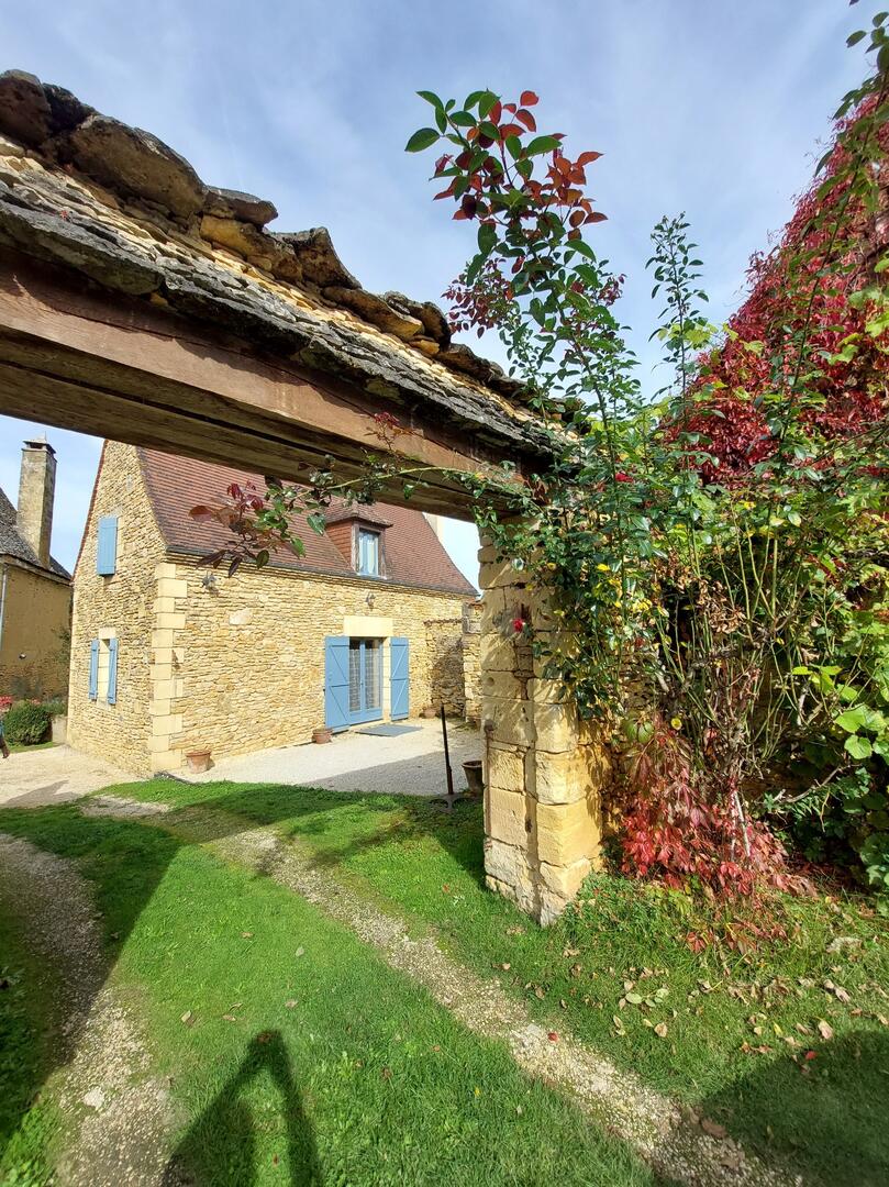Entrée extérieure du gîte, murs en pierre et végétation, location vacances Dordogne