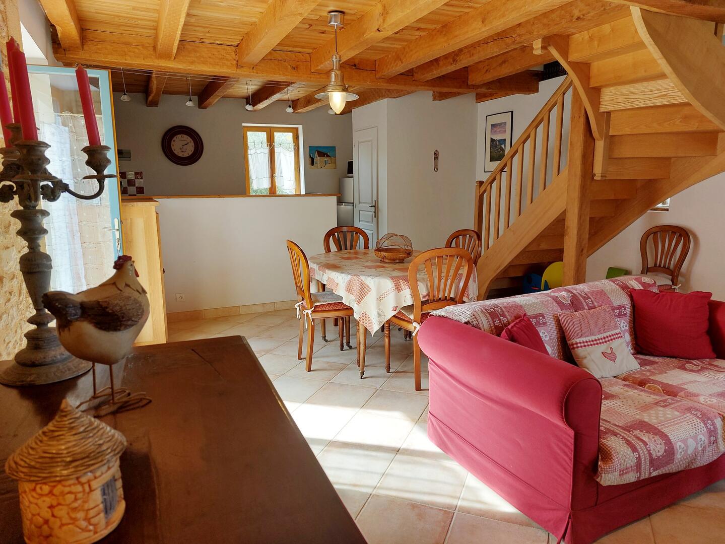 Salon lumineux avec canapé rouge, poutres apparentes et vue sur le jardin, gîte Dordogne